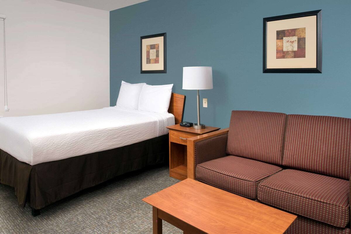 A hotel room with a bed, a sofa, a table, and two framed pictures on the wall.