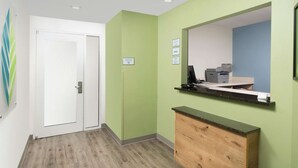 Un espace d’accueil avec un mur végétal, un comptoir en bois, un ordinateur et une imprimante.