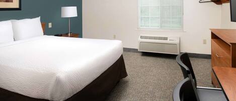 Une chambre d’hôtel avec un grand lit, un bureau, une chaise, une lampe, une fenêtre avec des stores et un appareil de climatisation.