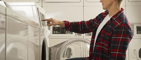 A person operating a front-loading washing machine in a laundromat with multiple machines.