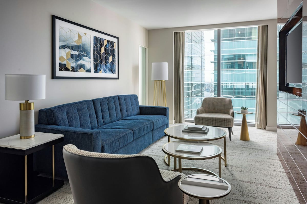 A modern hotel room with a blue sofa, a round coffee table, a chair, and a TV.