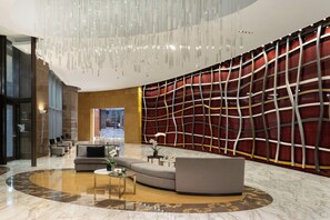 A modern lobby with a curved seating area, a large chandelier, and a red patterned wall. - JW Marriott Marquis Miami (Miami)