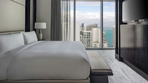 Camera d'albergo moderna con un letto grande, una lampada da comodino, una TV e vista sulla città e sull'oceano.