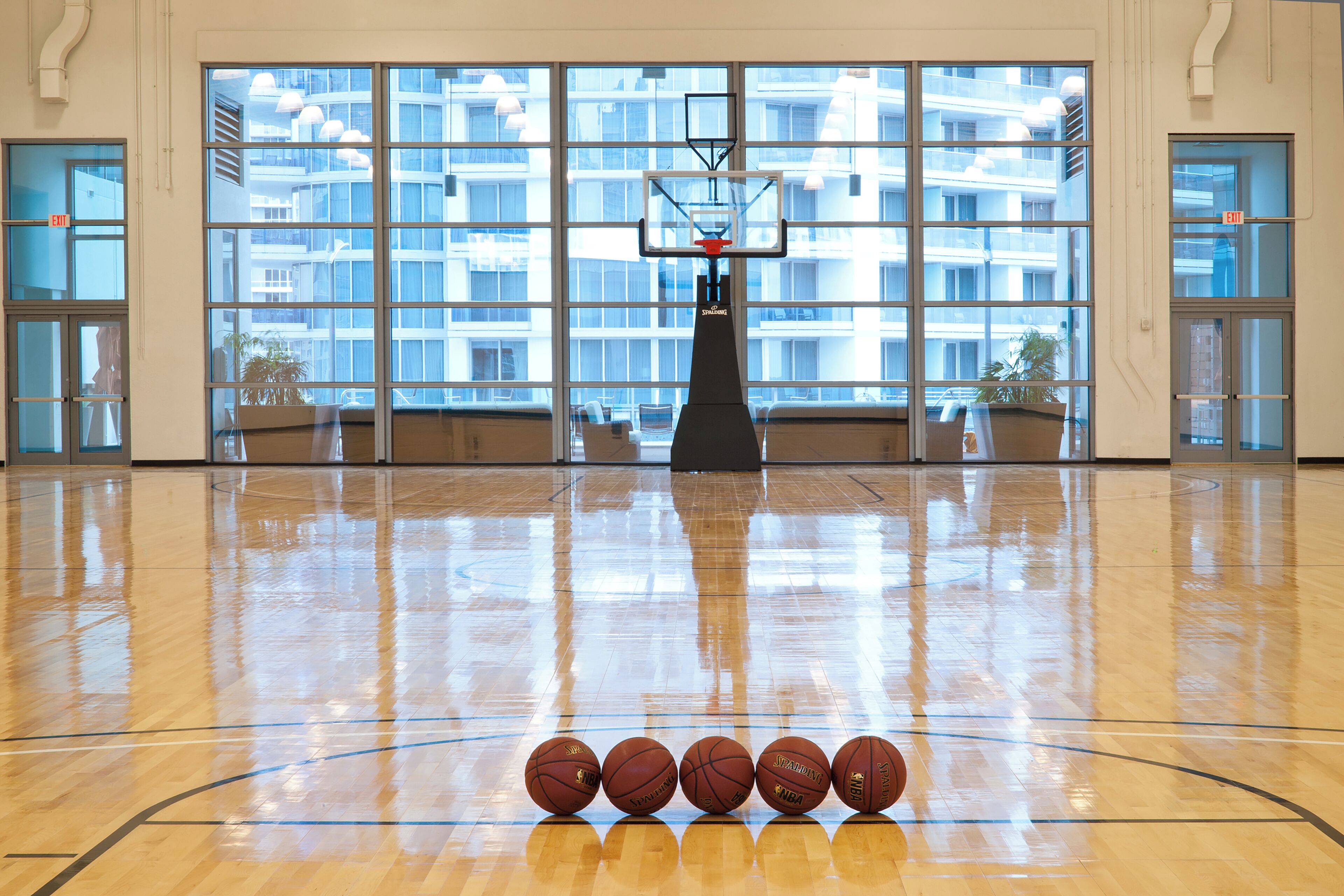 A basketball court with a hoop and five basketballs lined up in front.