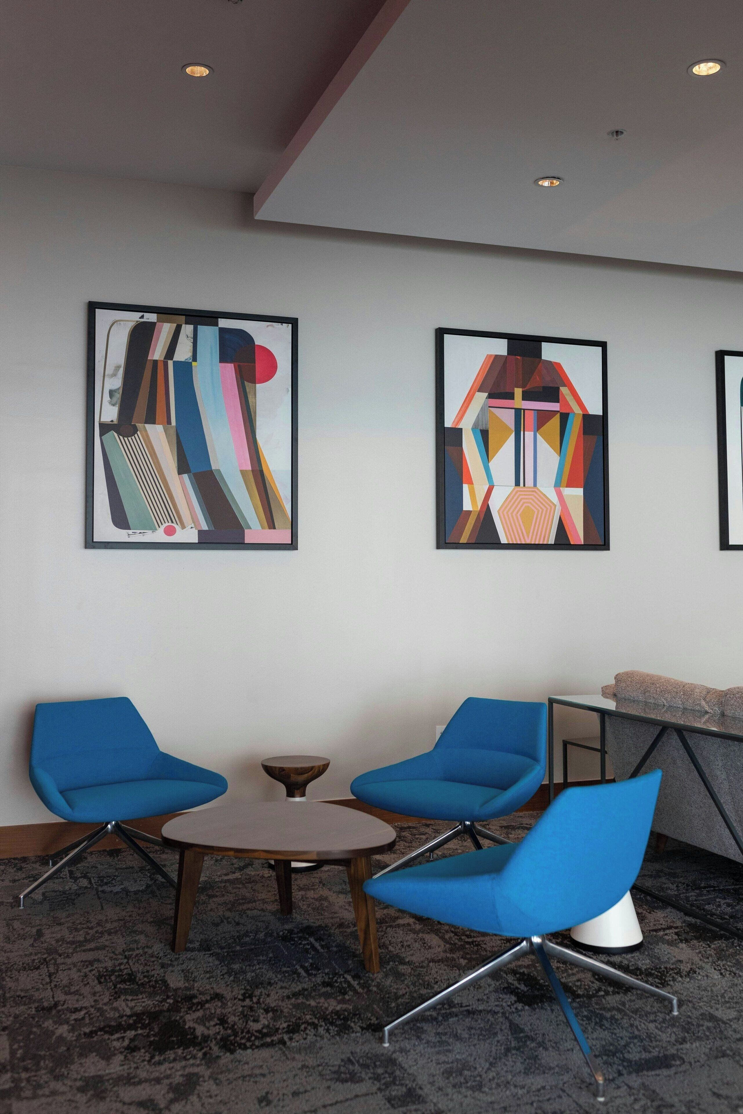 Una habitación moderna con dos sillas azules, una mesita redonda y arte abstracto en la pared.
