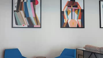 Una habitación moderna con dos sillas azules, una mesita redonda y arte abstracto en la pared.