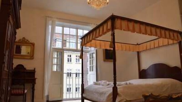 Una cama con dosel en una habitación con un ventanal grande, una araña y un espejo en la pared.