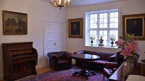 Una habitación con un piano, un sofá, una mesa redonda y una ventana con cortinas.