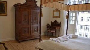 Un dormitorio con cama con dosel, un armario de madera, un escritorio con silla y una ventana con vista a edificios.
