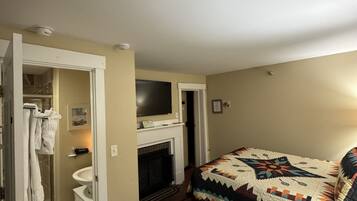 Un dormitorio con cama, chimenea, televisor y baño con inodoro y lavabo.