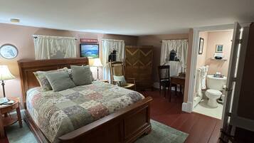 A bedroom with a wooden bed, a bedside table, a chair, a wardrobe, and a bathroom visible through an open door.