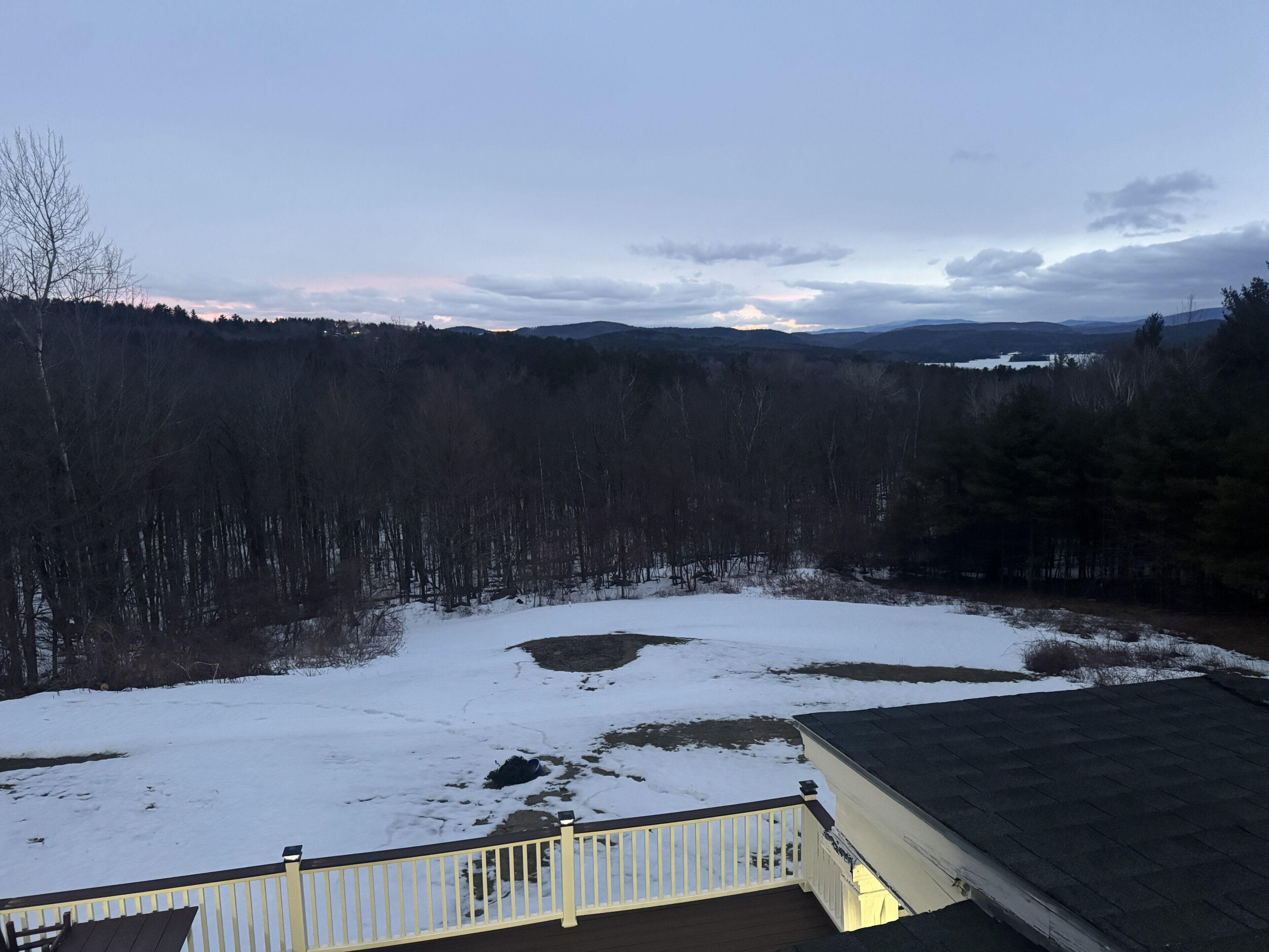 A snowy landscape with a view of a forest and distant hills.