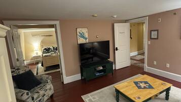 Una sala de estar con un sofá, una mesa de centro, un televisor sobre un mueble bajo, y una puerta que da a otra habitación.
