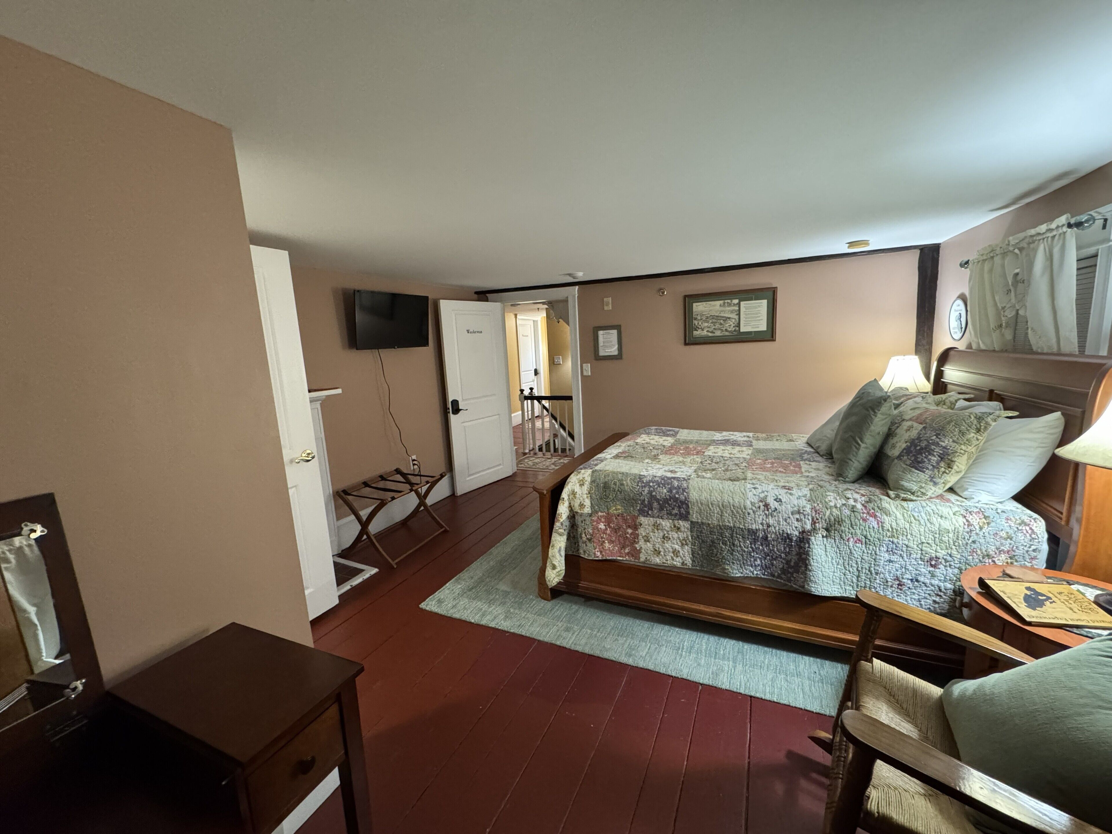 Un dormitorio con una cama, un escritorio, una silla, un televisor y una escalera que lleva a otra habitación.