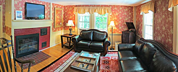 A living room with a fireplace, leather sofa, and a television. - The Ballard House Inn (Meredith)