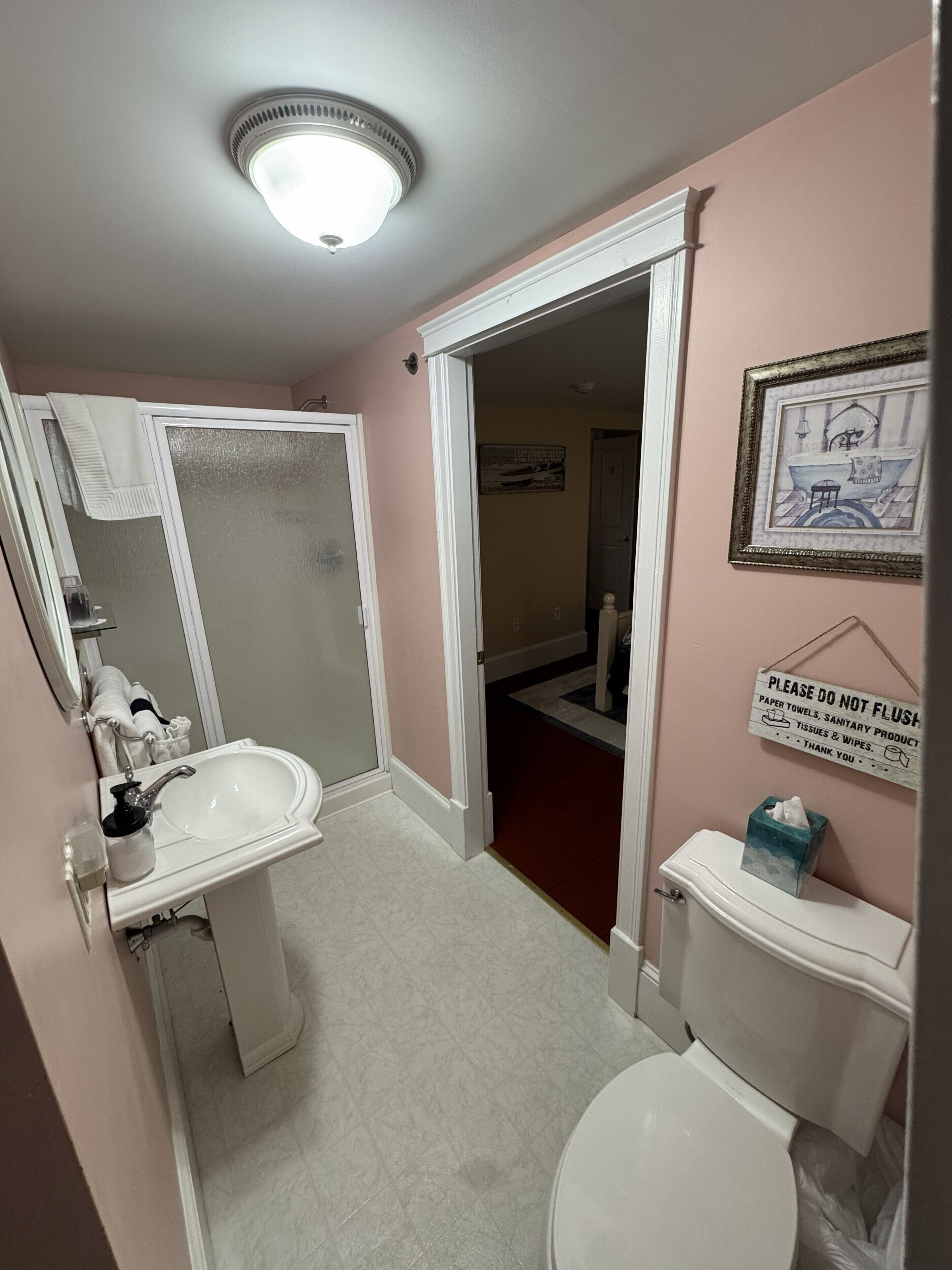 A bathroom with a sink, toilet, and shower. There is a sign on the wall advising not to flush paper towels, sanitary products, tissues, and wipes.