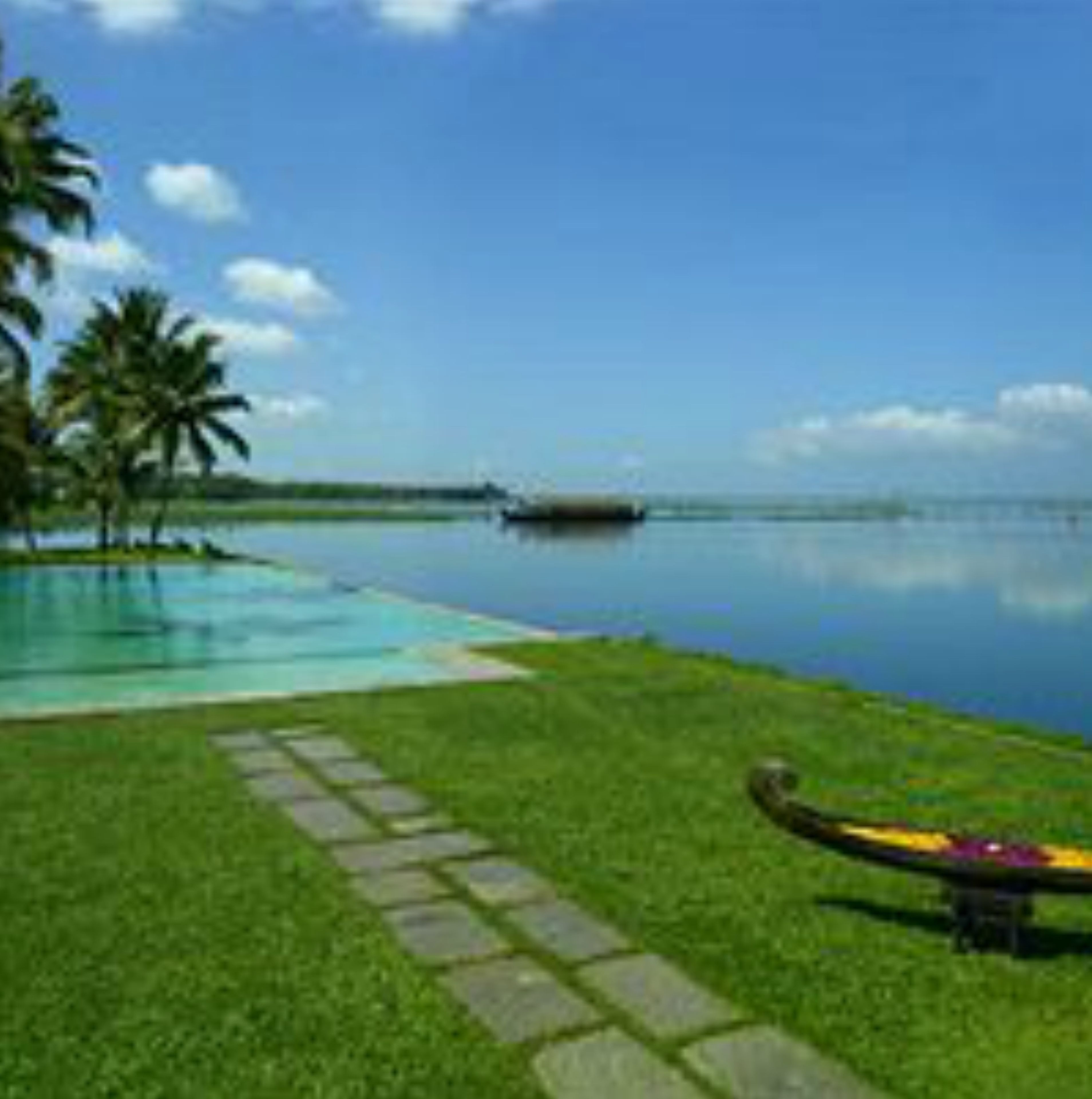 A serene pool area with a clear view of the water, a canoe, and palm trees.