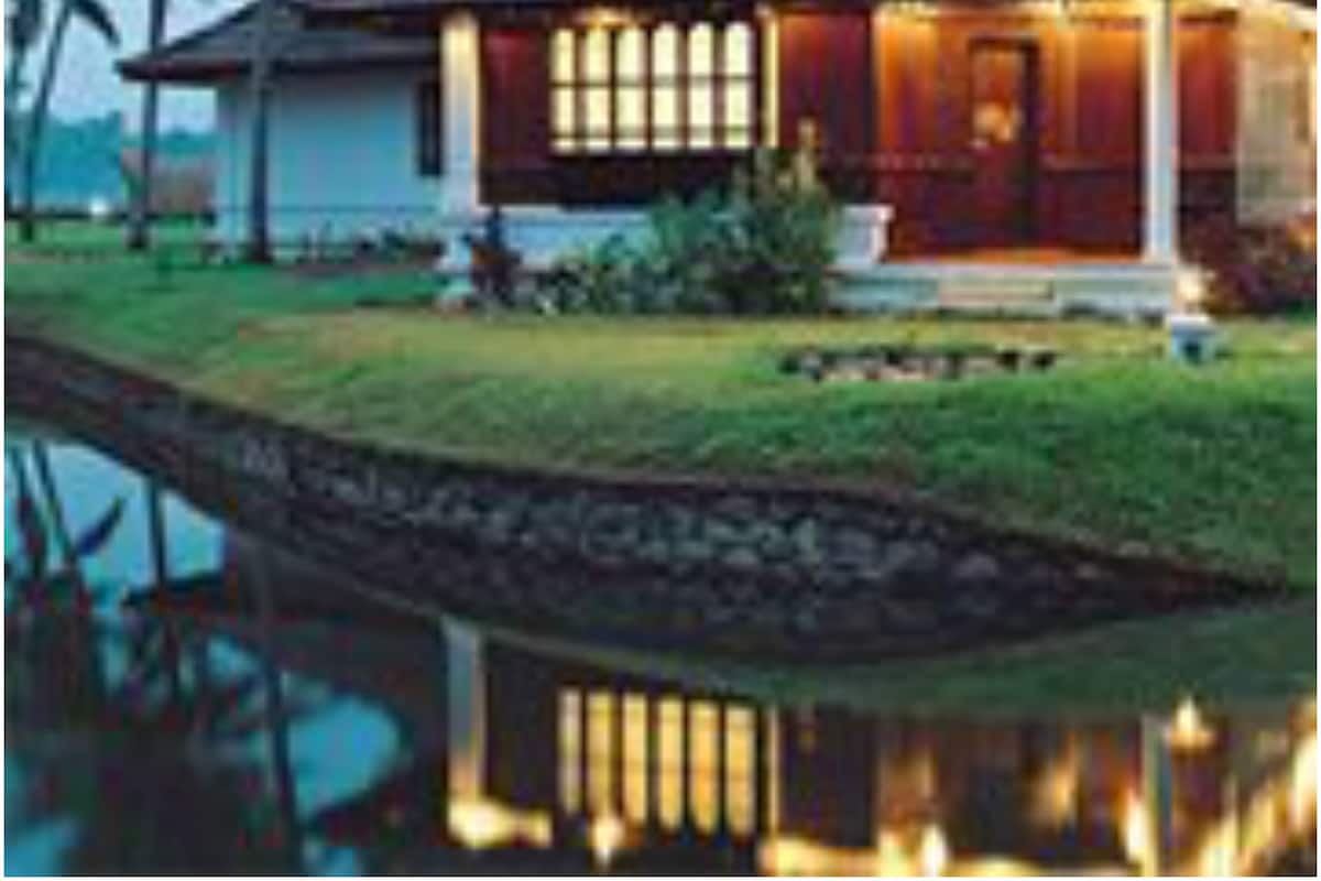 Ein traditionelles Haus mit Ziegeldach und Veranda, dessen Spiegelbild im Wasser zu sehen ist.