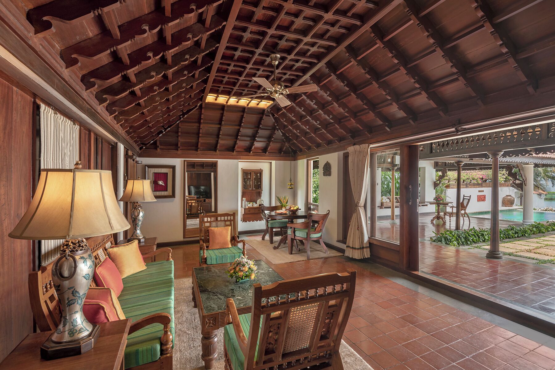 A spacious indoor area with a high ceiling, wooden ceiling beams, and a view of a pool outside.