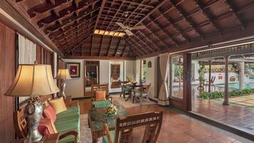 A spacious indoor area with a high ceiling, wooden ceiling beams, and a view of a pool outside.