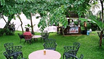 An outdoor seating area with metal chairs and a table, surrounded by lush greenery and a view of the sea.