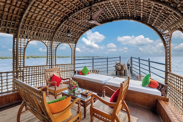 Cubierta de barco con mobiliario de madera, una mesa con un jarrón de flores y vista al agua.