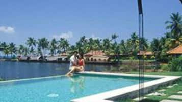 A clear blue pool with a person sitting on the edge, surrounded by palm trees and a clear sky.