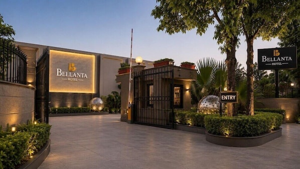 The exterior of the Bellanta Hotel with a well-lit entrance, a gated entry, and landscaped areas. - Mapple Emerald (New Delhi)