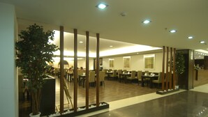 Un hall d’hôtel spacieux au design moderne, agrémenté d’une grande plante en pot, de colonnes en bois et d’un sol ciré.