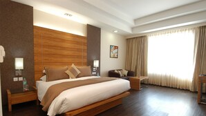 Une chambre d’hôtel spacieuse, dotée d’un grand lit, de tables de chevet, d’un bureau et d’une fenêtre avec des rideaux.