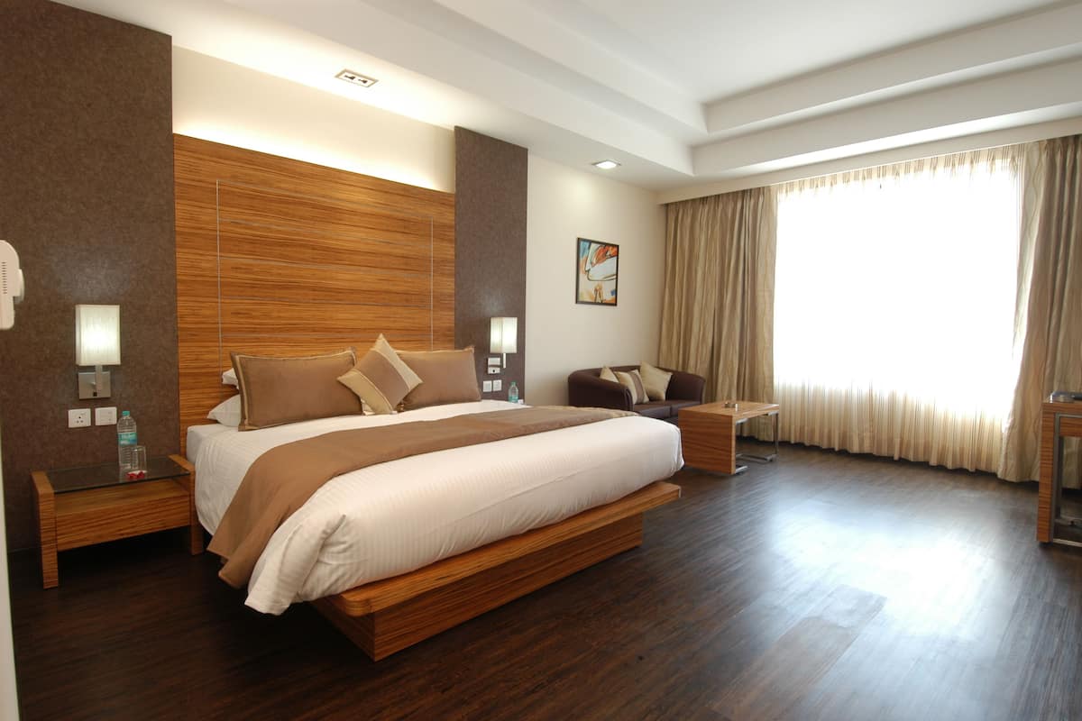 A spacious hotel room with a large bed, bedside tables, a desk, and a window with curtains.