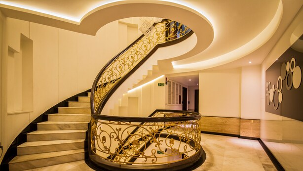 A grand spiral staircase with ornate golden railings, marble steps, and a modern ceiling design. - Hotel Grand Godwin near the New Delhi railway station & Connaught Place. (New Delhi)