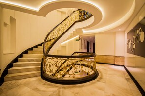 A grand spiral staircase with ornate golden railings, marble steps, and a modern ceiling design. - Hotel Grand Godwin near the New Delhi railway station & Connaught Place. (New Delhi)