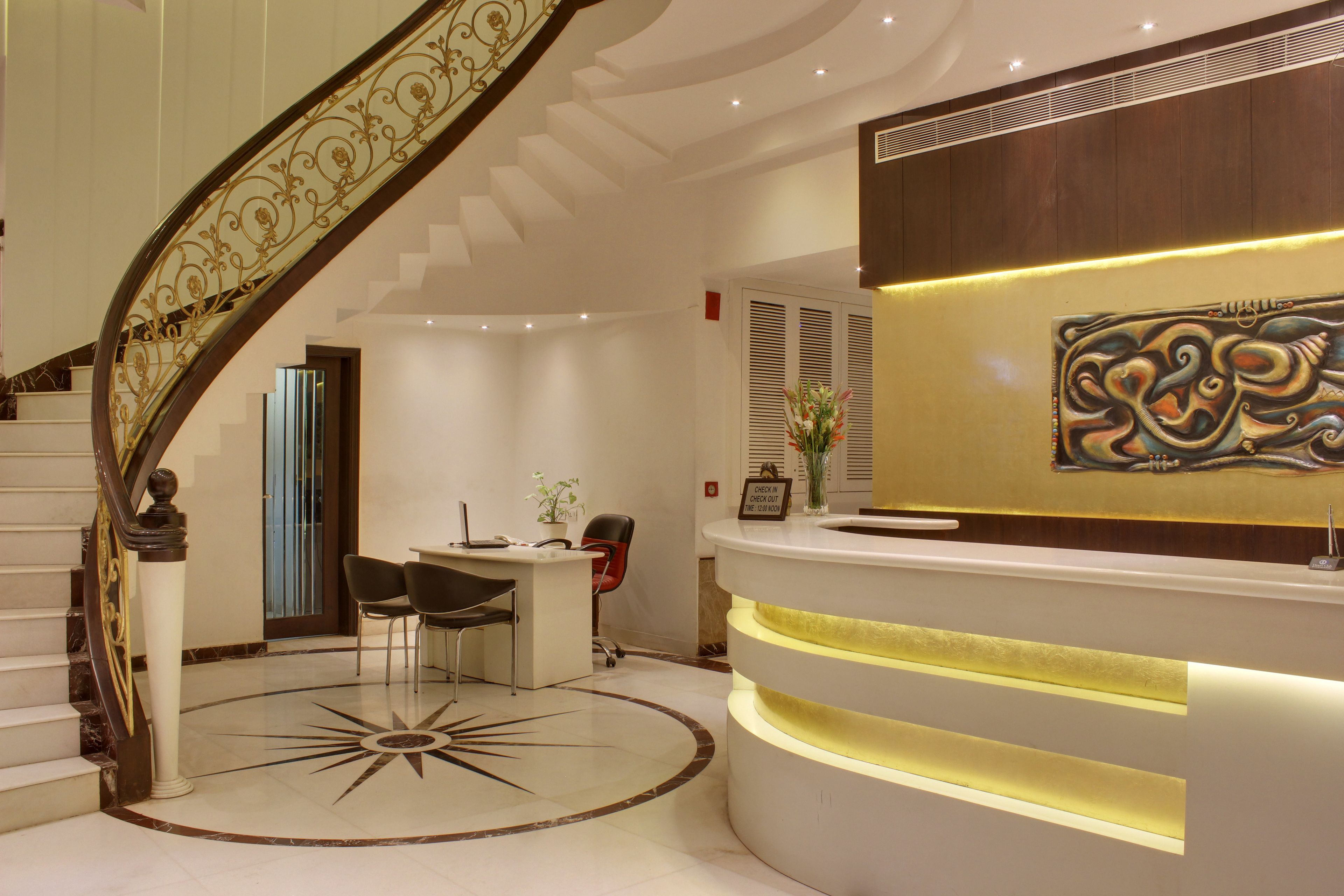 A reception area with a curved desk, a staircase with ornate railings, and a decorative wall piece.