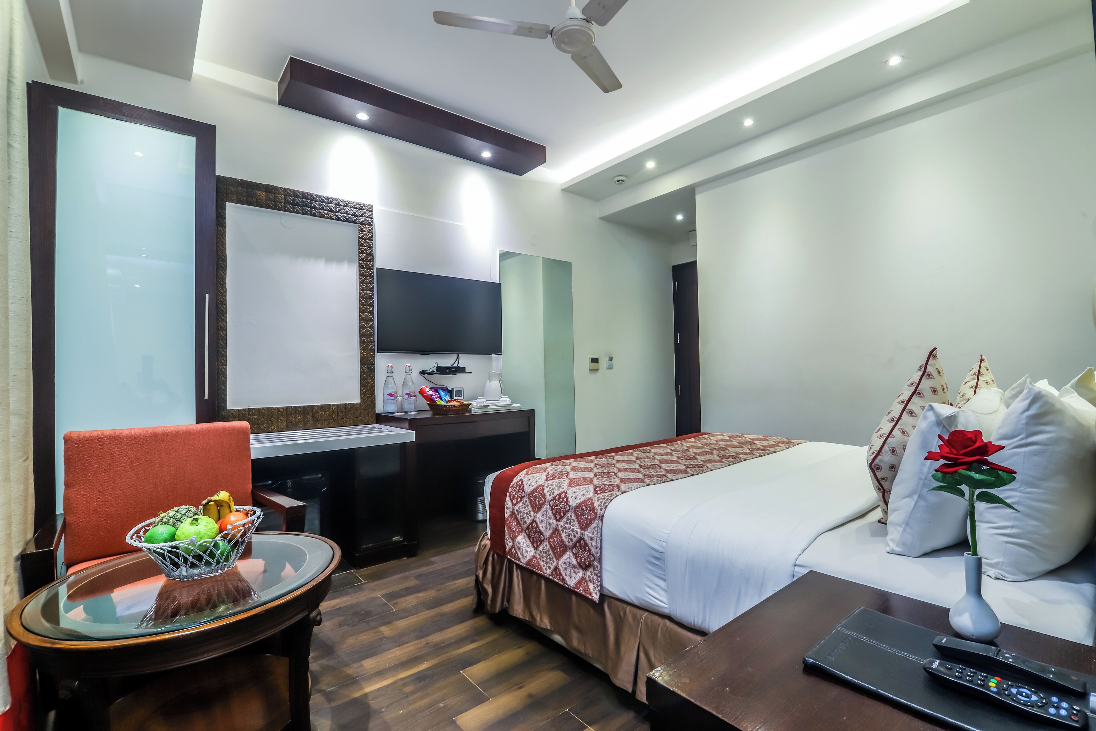 Habitación de hotel con cama, escritorio, silla, una mesita con frutero, un florero con una flor y un control remoto.