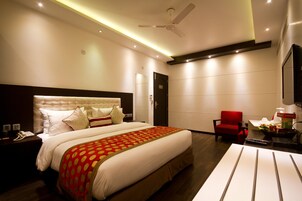 Een moderne hotelkamer met een groot bed, een rode fauteuil, een bureau met lamp en een plafondventilator.