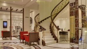 A modern lobby with a marble floor, a spiral staircase, red seating, and a reception area. - Hotel Grand Godwin near the New Delhi railway station & Connaught Place. (New Delhi)