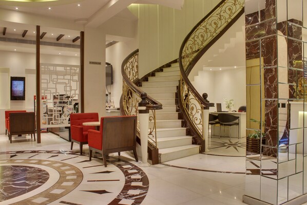 A modern lobby with a marble floor, a spiral staircase, red seating, and a reception area. - Hotel Grand Godwin near the New Delhi railway station & Connaught Place. (New Delhi)