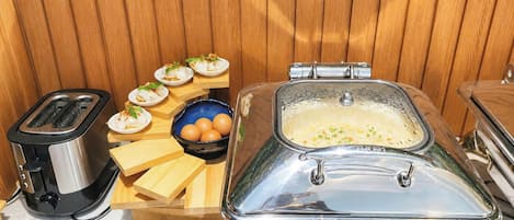 A kitchen area with a toaster, a food station with plates of food, a bowl of eggs, and a large metal container.