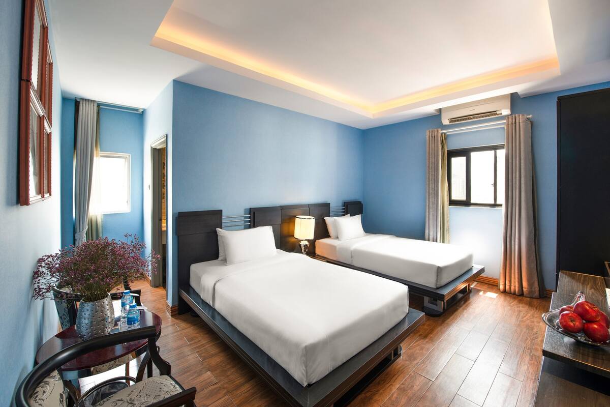 Ein Hotelzimmer mit zwei Betten, einem Schreibtisch, einem Stuhl, einer Vase mit Blumen und einer Obstschale.