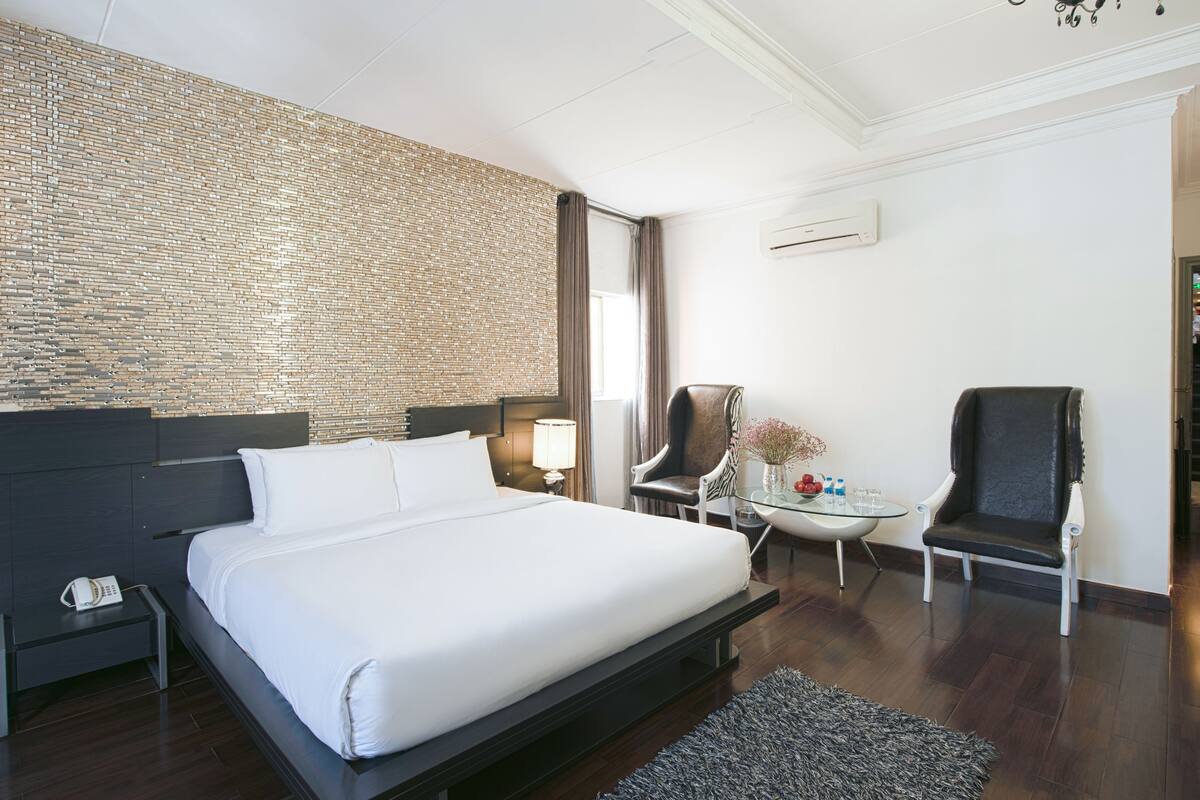 Ein modernes Hotelzimmer mit einem großen Bett, einer Wand mit Ziegeln, einem kleinen Tisch mit einer Vase und zwei Stühlen.