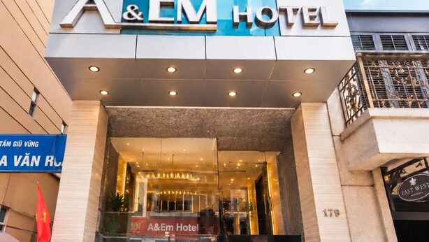 The exterior of the A&EM Hotel with a modern facade, large glass windows, and a prominent entrance with a staircase. - A&EM - The Petit Hotel (Ho Chi Minh City)