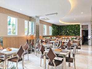 Ein geräumiges Restaurant mit mehreren Tischen und Stühlen, einem modernen Deckenstil und einer begrünten Wand mit Pflanzen.