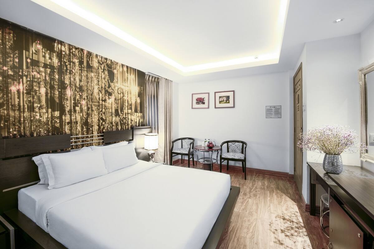 Ein Hotelzimmer mit einem großen Bett, einem Schreibtisch mit Stuhl, einem kleinen Tisch für zwei Personen und einem großen Kunstwerk an der Wand.