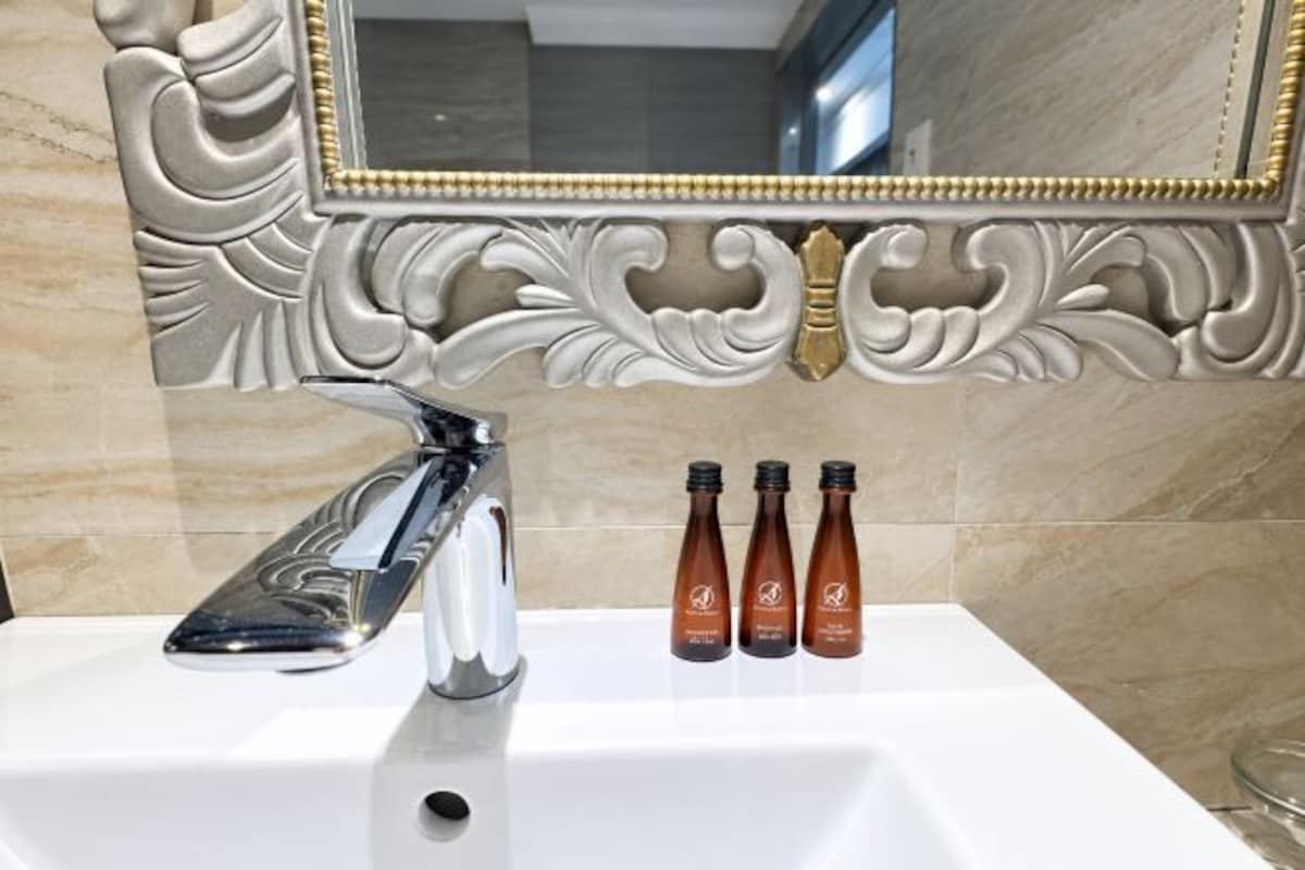 A bathroom sink with a modern faucet, a mirror with ornate detailing, and three bottles of brown liquid.