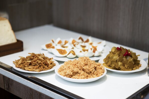 Une table de buffet proposant divers plats, notamment des aliments frits, une assiette de légumes coupés en tranches et un plat agrémenté d’une garniture rouge.