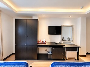 A hotel room with a bed, a desk with a chair, a wardrobe, a television, and a mirror.