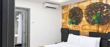 A hotel room with a bed, a wall-mounted air conditioner, and a decorative wall piece.