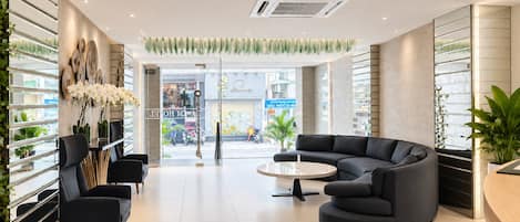 A modern hotel lobby with a curved sofa, a round coffee table, and a reception desk.