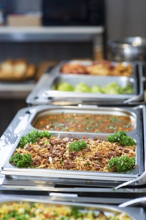 Un buffet proposant divers plats, notamment des nouilles et de la viande, présentés sur des plateaux en métal.